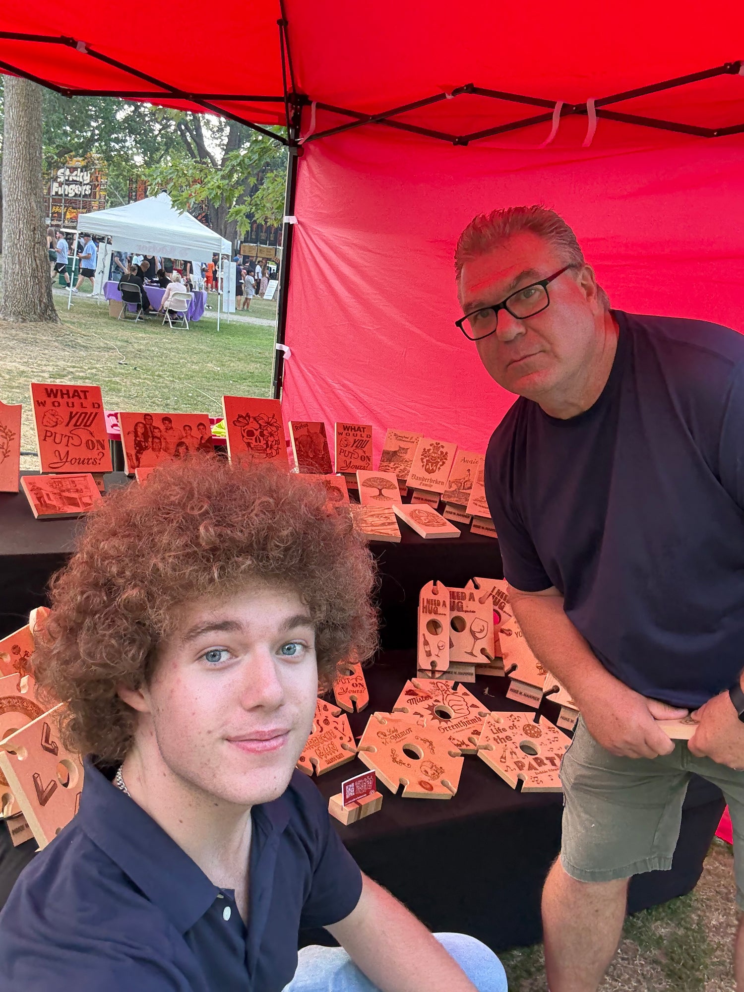 Mike and Talon standing under a red tent with a table displaying beautiful wood products.